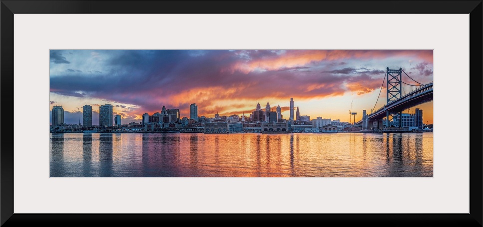Panoramic view of a fiery sunset over the Philadelphia city skyline, with the Benjamin Franklin Bridge on the right.