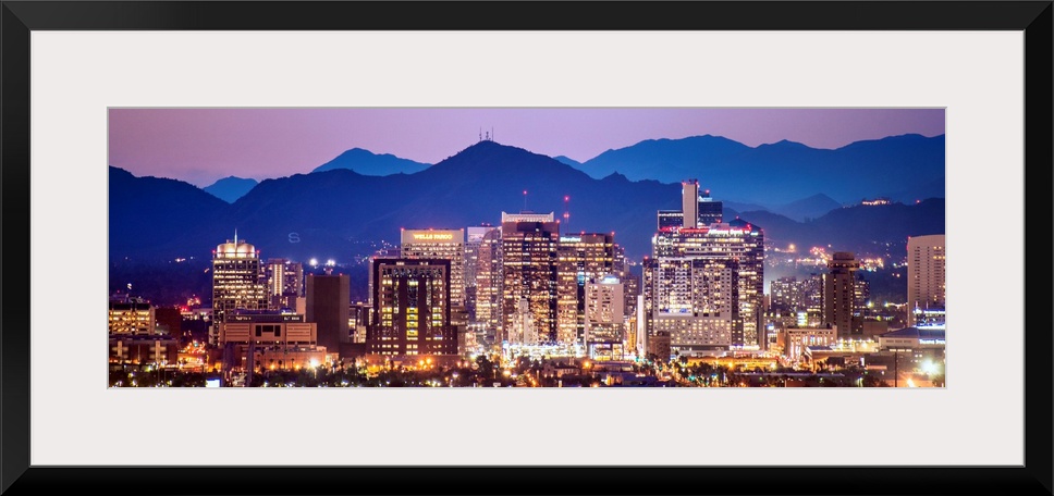 Panoramic photograph of a colorful sunset over the Phoenix, Arizona skyline with silhouetted mountains in the background.