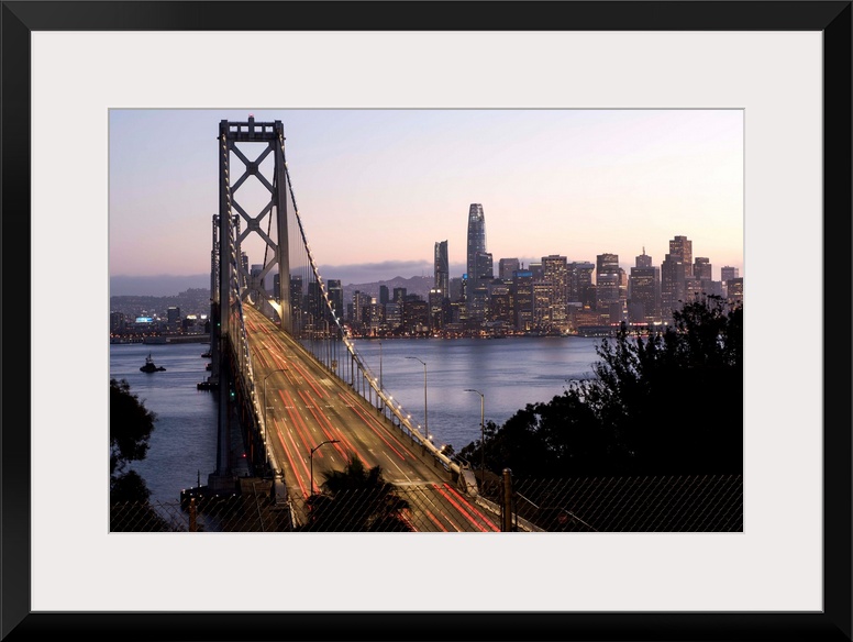 Photograph of the Bay Bridge with a pink and purple sunset and the San Francisco skyline lit up in the background.