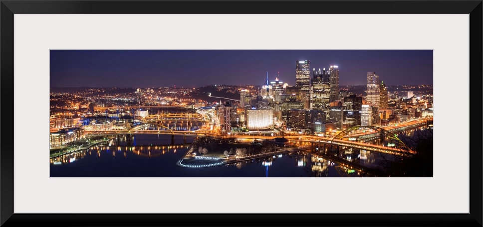 Panoramic photo of the city of Pittsburgh illuminated at night, with Point State Park in the foreground.