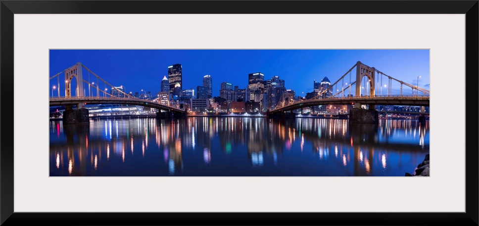 Panoramic view of the Pittsburgh city skyline in the evening reflected in the water, with two of the Three Sisters bridges...