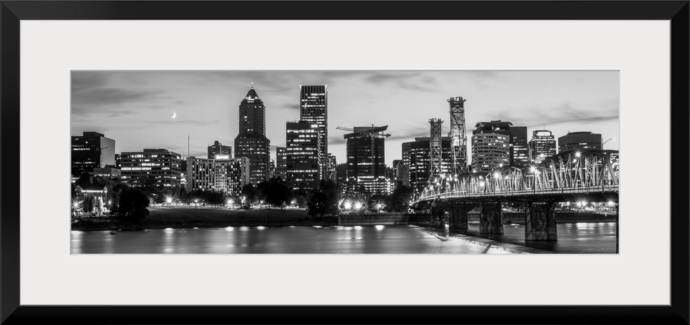 Panoramic photograph of the Portland, Oregon skyline lit up with lights at the beginning of sunset with a small crescent m...