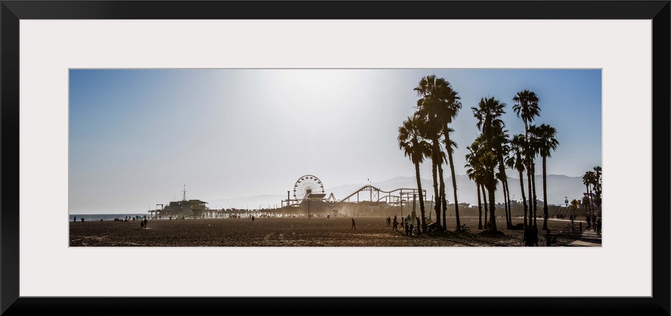 Panoramic photograph of the Santa Monica Pier in Los Angeles, California, with palm trees in the foreground and a purple h...