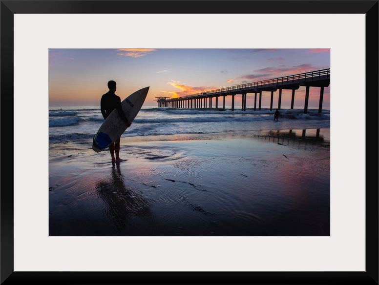 Silhouetted photograph of a man holding a surf board on the shore of Ocean Beach in San Diego, California, with the Ocean ...