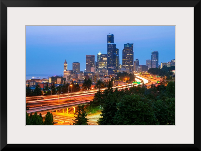 Photograph of the Seattle skyline at dusk with light trails from the cars on the highway in the foreground.