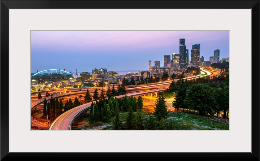 Panoramic photograph of the Seattle skyline at night with light trails from the car lights on the highway.