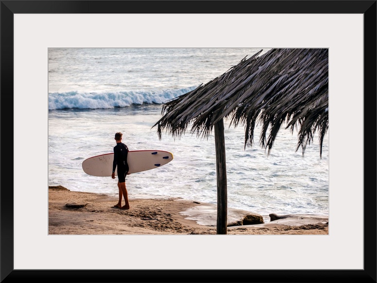 Photograph of a surfer walking along the shore of the pacific ocean in San Diego, California, with a cabana built with nat...