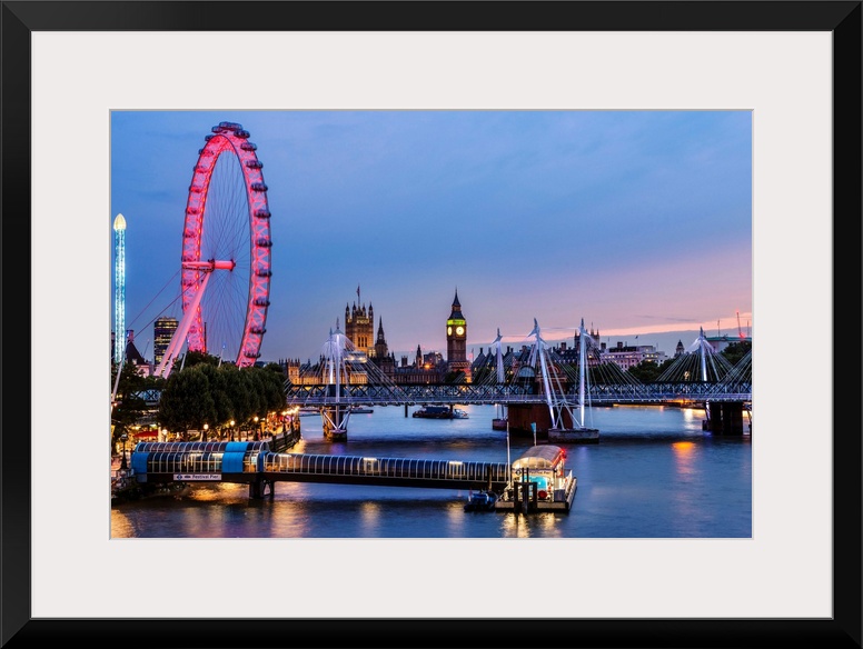 Photograph of the London Eye lit up at night with Big Ben in the background and the Golden Jubilee Bridge going over River...