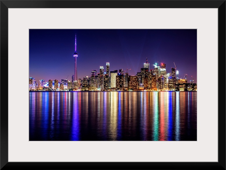 Photo of the Toronto city skyline with lights reflected in the water at night.