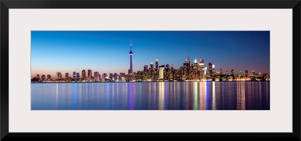 Panoramic photo of the Toronto city skyline with lights reflected in the water at night.