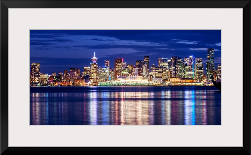 Photograph of the Vancouver, British Columbia skyline lit up on a dark blue night and reflecting bands of colorful light o...