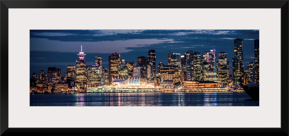 Panoramic photograph of the Vancouver, British Columbia skyline lit up on a dark blue night and reflecting bands of colorf...