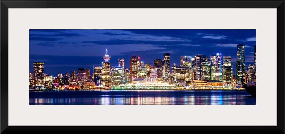 Panoramic photograph of the Vancouver, British Columbia skyline lit up on a dark purple night and reflecting bands of colo...