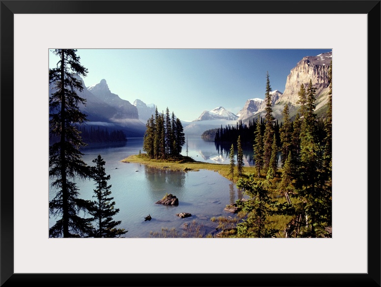 Large wall print of a forest of evergreens meeting and jutting out into a clear lake surrounded by rugged mountains.