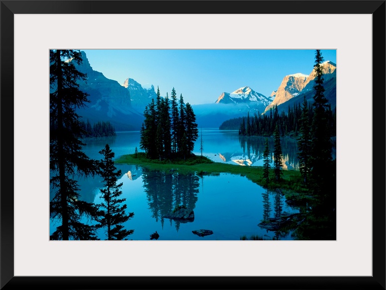 The northern landscape of evergreen trees and mountains reflect on the still waters of a lake in the morning.