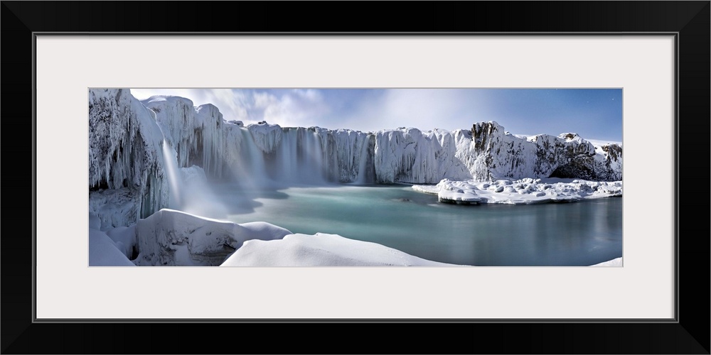 Icy snow covered landscape with waterfalls streaming down from cliffs surrounding a river.