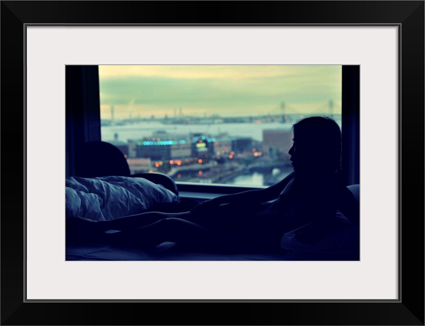 A portrait of a nude woman lying in a bed with a blue light coming through a window with a harbor scene outside.