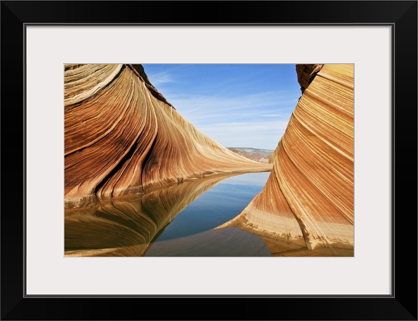 Striated rock formations in Vermilion Cliffs National Monument, reflected in the water of a stream.