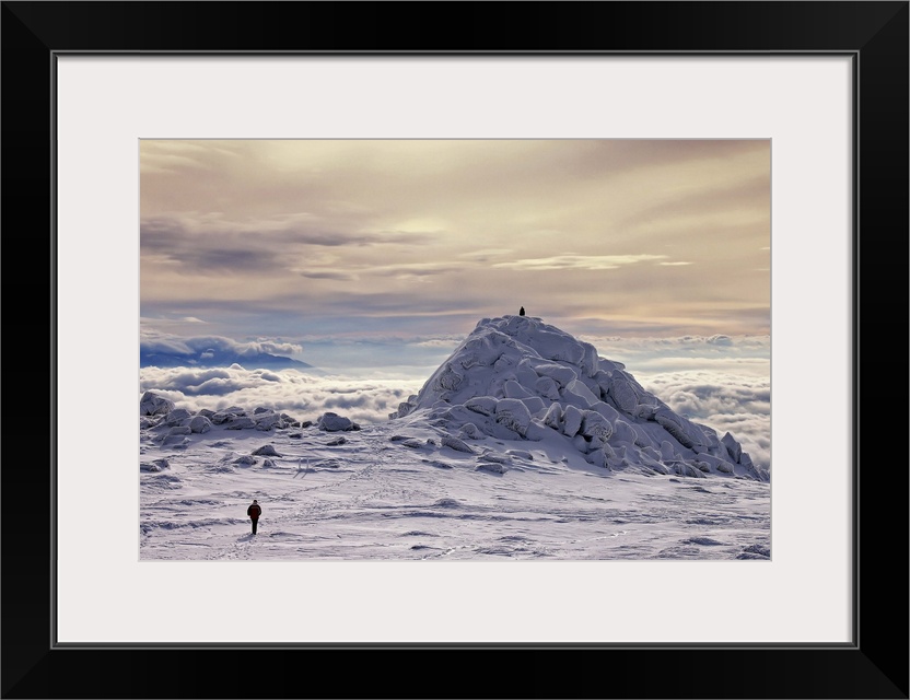 A figure walks across a snowscape on a mountain top, with another figure on a hill in the distance, a sea of clouds below.