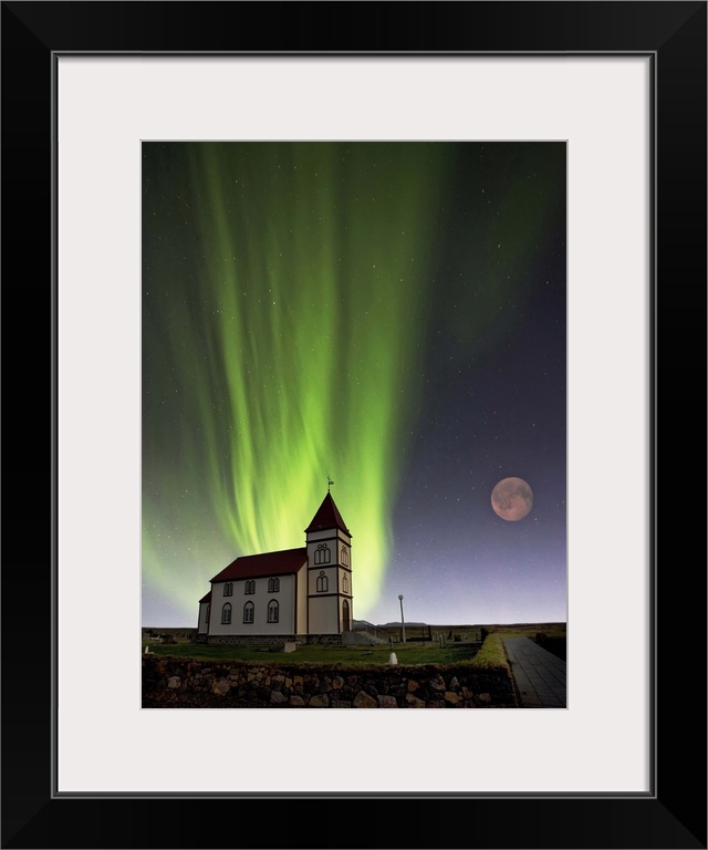 A church with a red roof and the lights of the aurora borealis glowing in the sky overhead, with a full moon.