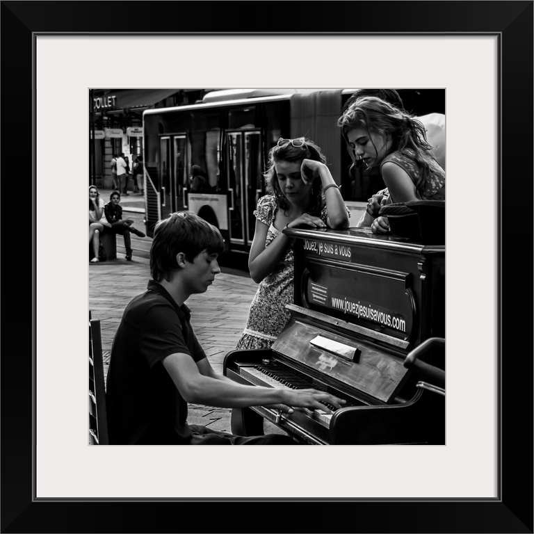 A black and white photograph of a man playing a piano in the street and women sitting around listening.