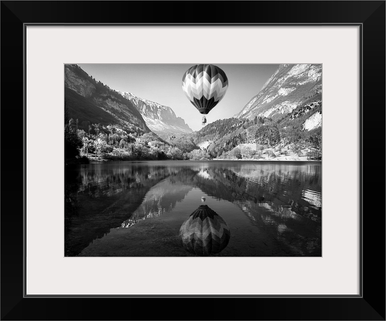 Hot air balloon rising above a lake in the mountains, with its mirror reflection below.