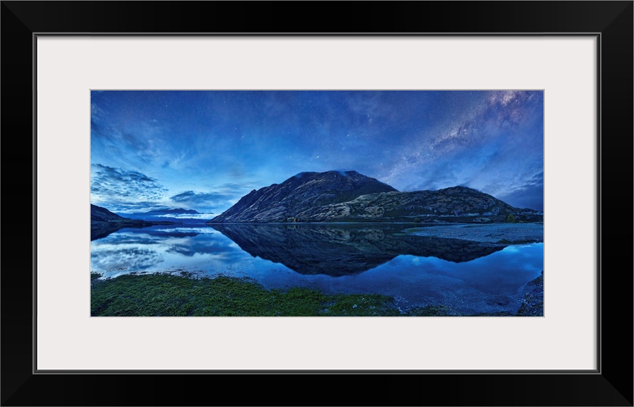 A crystal blue lake reflects its mountainous environment under starry night sky, New Zealand.