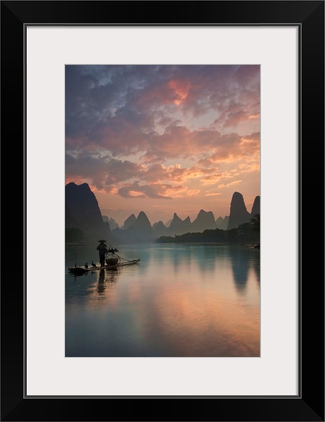 A fisherman on a boat in the Li River, with beautifully colored clouds at sunrise, China.