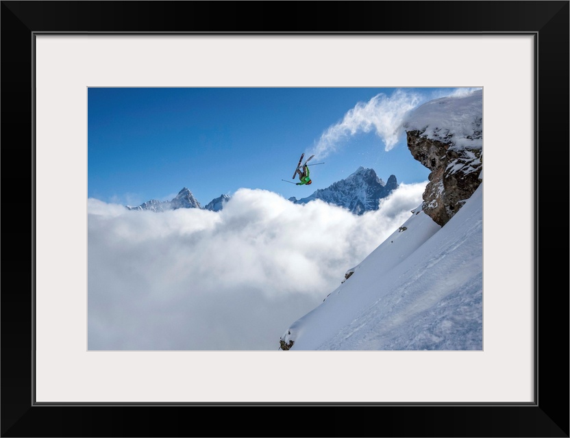 A skier leaps off a mountain in France, kicking off snow from the ends of the skies.