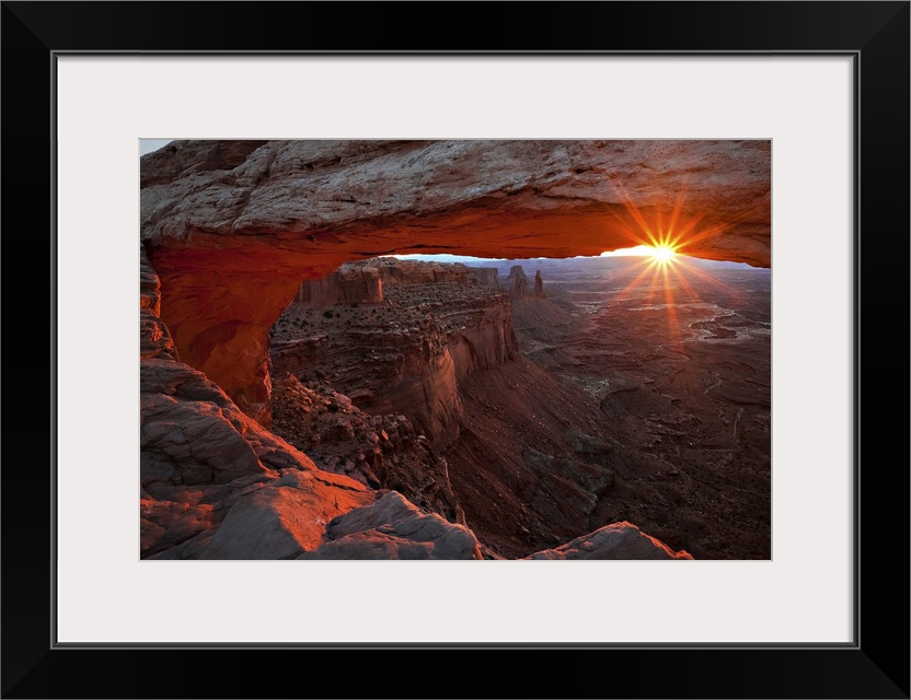 The sun framed by a large natural arch and the horizon, Canyonlands National Park, Utah.