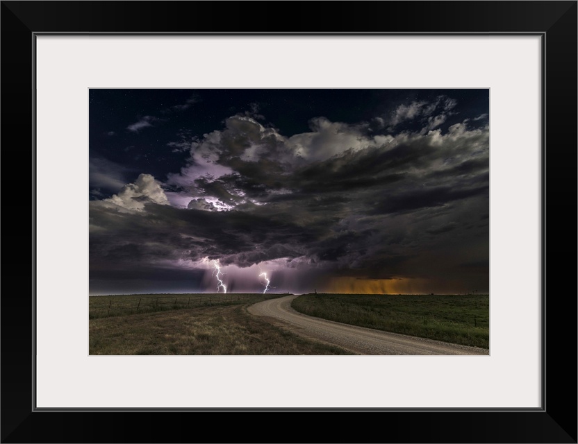 Dramatic clouds throw down bright purple bolts of lightning on a prairie landscape.