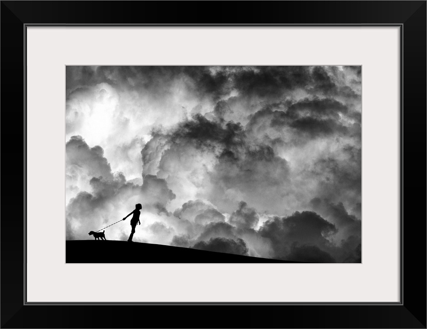 A girl holding a dog on a leash in silhouette against a background of dramatic clouds.