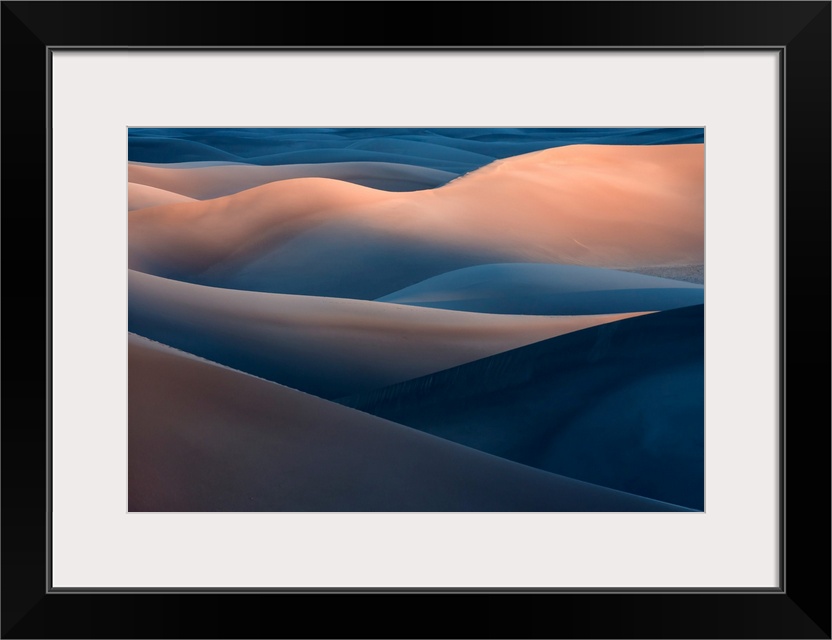 A desert landscape with tall blue and orange sand dunes in the evening.