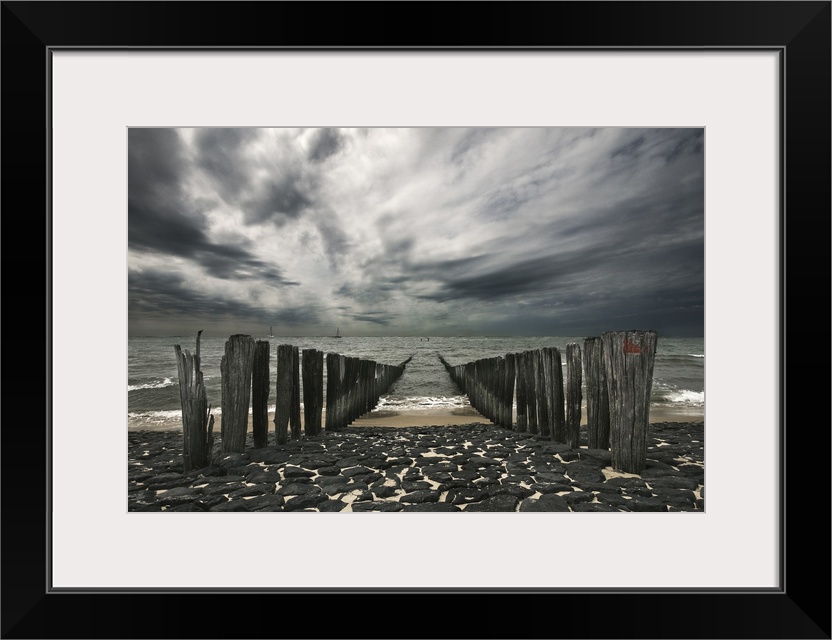 Landscape photograph of the ocean and the remains of a pier on an overcast, gloomy day.