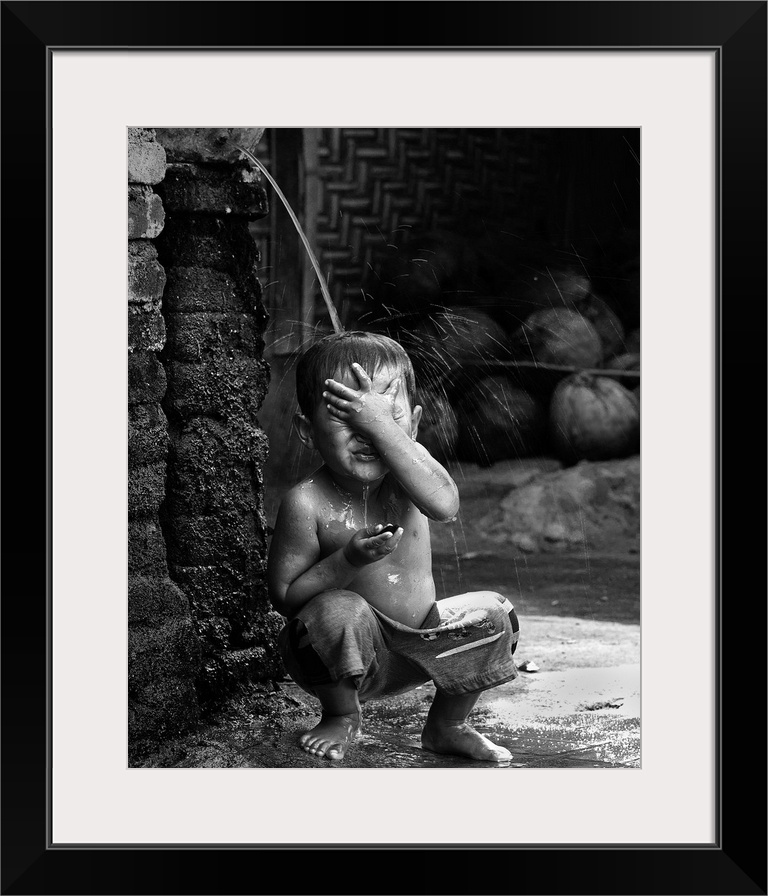 A young boy sits under a stream of water in the village of Sade, Lombok, Indonesia.