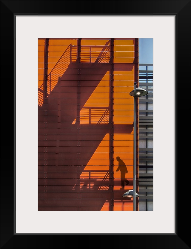 Shadow of a fire escape staircase and a person walking down cast onto the side of an orange building.