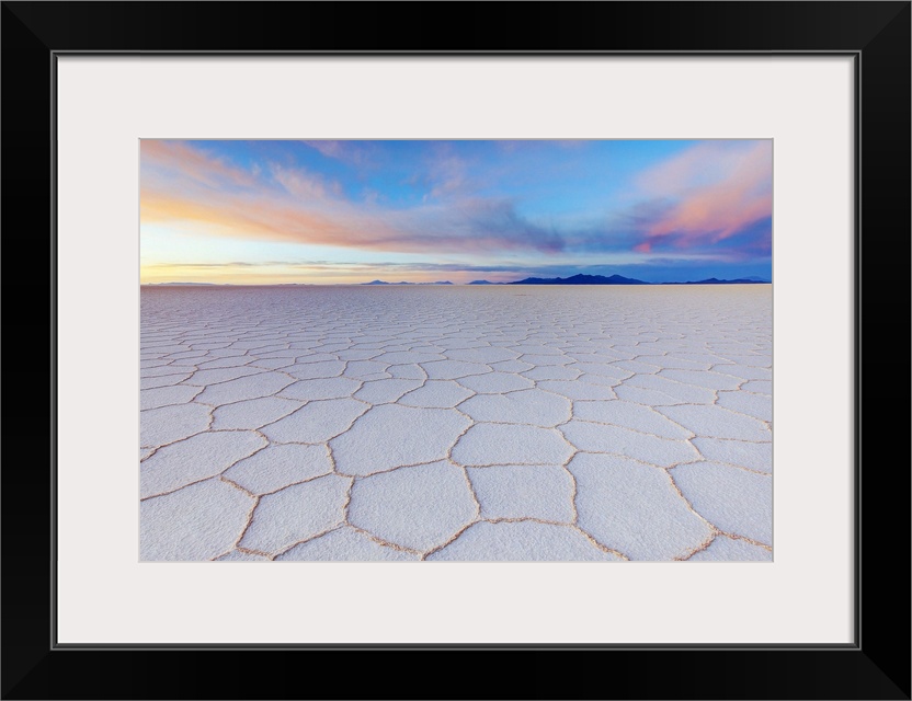 Cracked earth in the salt flats of Bolivia with pastel colors in the sky from the sunrise, Tanupa volcano in the distance.