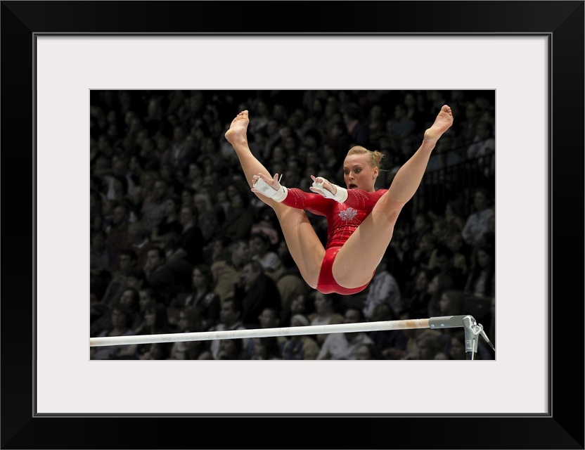 A female gymnast flies over the high bar with her legs raised up, arms outstretched ready to grab the bar.