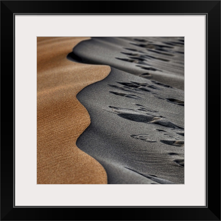 Two opposing sides of a sand dune, one smooth and orange, the other grey and full of footprints.