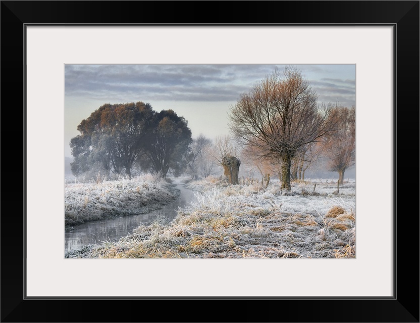 Frost-covered field with a stream and trees, Poland.