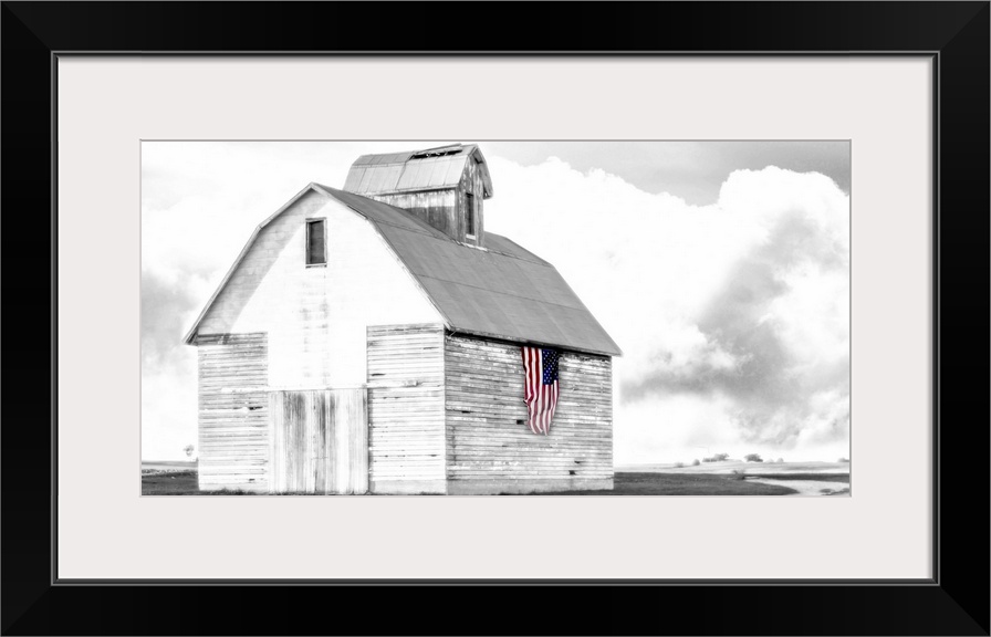An image of a barn in black and white with an american flag on the side of the building in color.