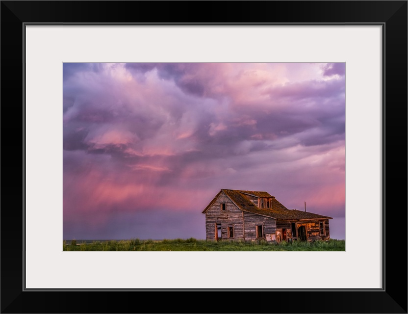 Abandoned barn on farmland with storm clouds glowing pink; Val Marie, Saskatchewan, Canada