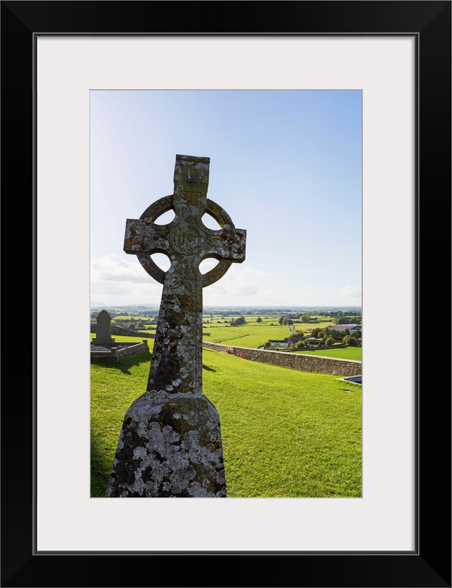 Celtic cross on grassy hill with stone wall under blue sky, Cashel, County Tipperary, Ireland.