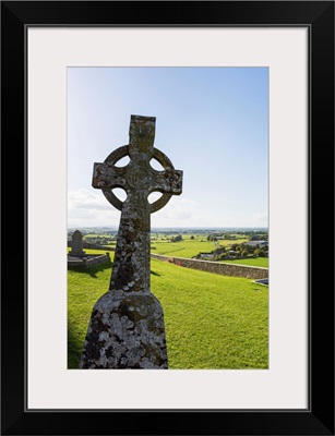 Celtic cross on grassy hill with stone wall under blue sky, Cashel, Ireland
