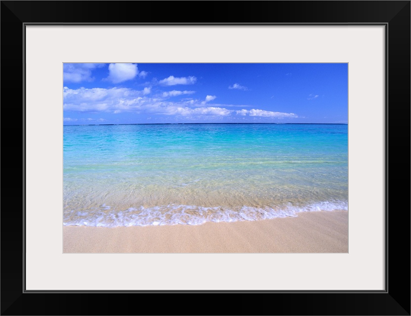 This home docor features a photograph that is a horizontal seascape of clean ocean water washing up on a sandy beach.