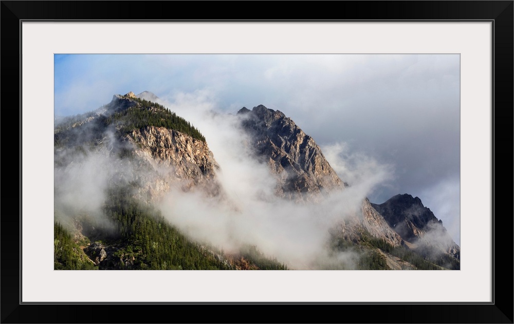 Clouds gather around rocky mountain peaks, field, British Columbia, Canada.