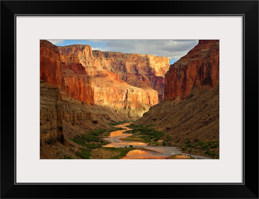 Large wall art of a river winding through the bottom of the Grand Canyon while the sides of the canyons cast shadows in th...