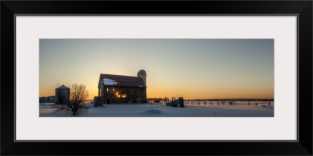 Dilapidated bard at sunrise in winter with a glowing yellow sky over the horizon seen through the abandoned barn, Rudyard,...