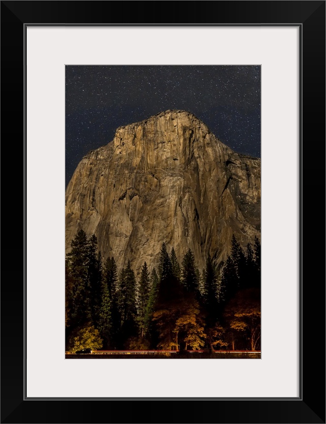 A vehicle drives along Northside Drive in front of El Capitan at night in Yosemite Valley, Yosemite National Park. Califor...