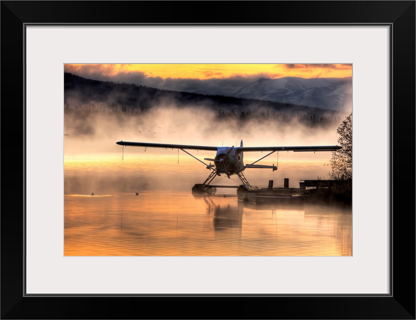 Giant photograph displays a seaplane sitting next to a dock as a soft fog rolls over the water.  In the background, the fa...